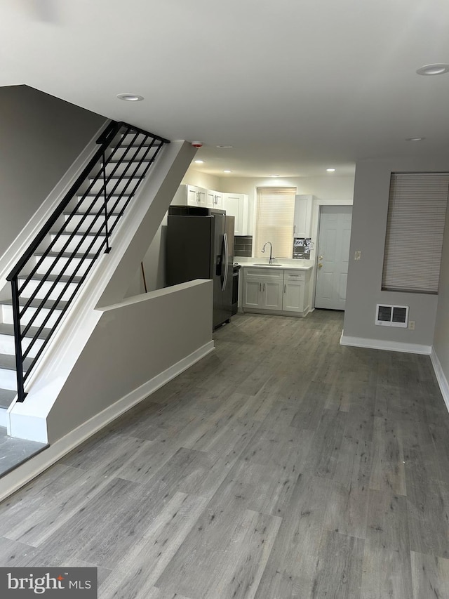 unfurnished living room featuring light wood-style floors, visible vents, stairway, and baseboards