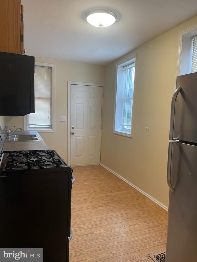 kitchen featuring sink, gas stove, stainless steel refrigerator, and light wood-type flooring