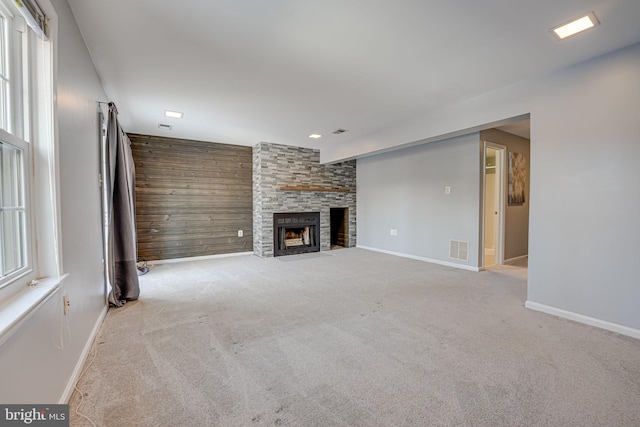 unfurnished living room with a fireplace, light colored carpet, and wood walls