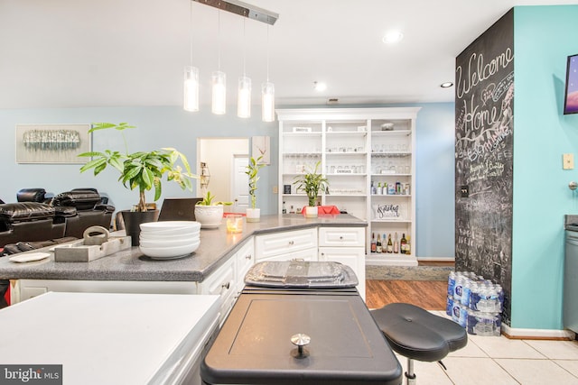 kitchen with a breakfast bar area, white cabinetry, light tile patterned flooring, and hanging light fixtures