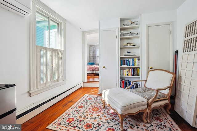 living area with a wall unit AC, baseboard heating, and hardwood / wood-style floors