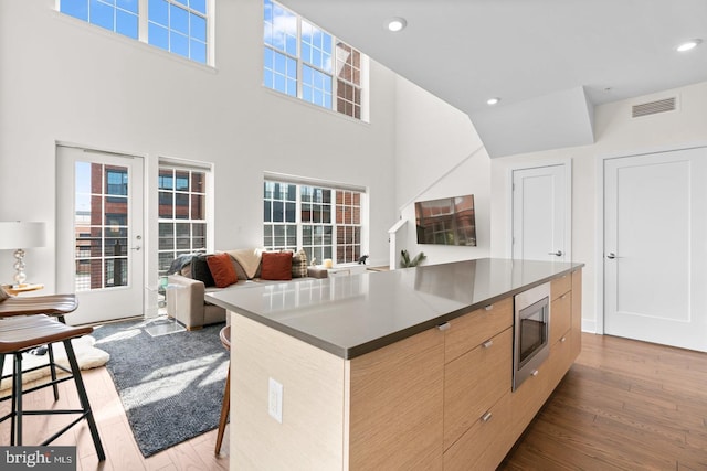 kitchen featuring a kitchen island, stainless steel microwave, light wood-type flooring, and light brown cabinetry