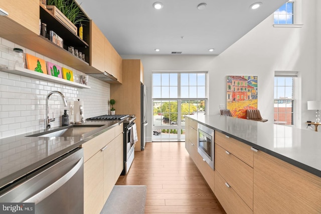 kitchen with light brown cabinets, sink, decorative backsplash, light wood-type flooring, and appliances with stainless steel finishes