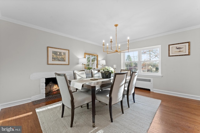 dining space featuring radiator, a premium fireplace, dark hardwood / wood-style flooring, a chandelier, and ornamental molding