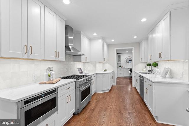 kitchen with hardwood / wood-style floors, wall chimney range hood, decorative backsplash, white cabinetry, and stainless steel appliances