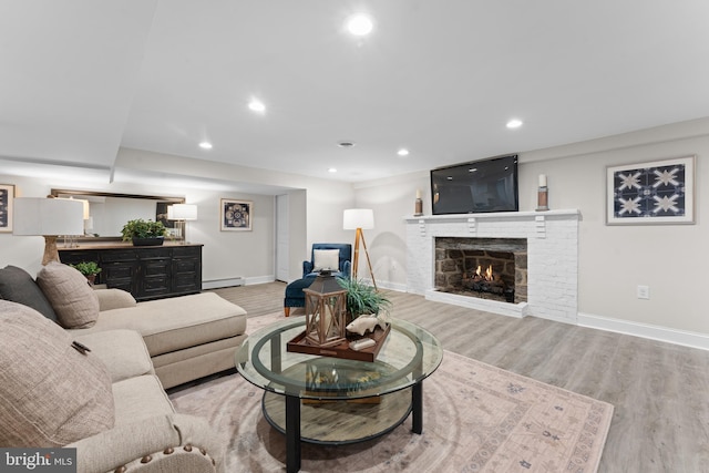 living room featuring light hardwood / wood-style floors, a brick fireplace, and a baseboard radiator