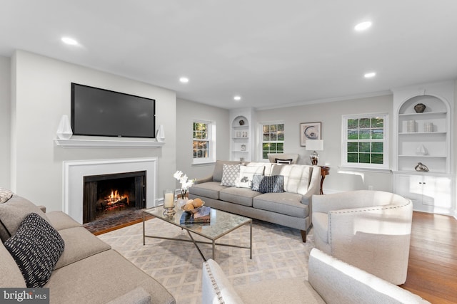 living room featuring built in shelves, light wood-type flooring, and crown molding