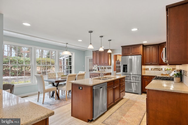 kitchen with a center island with sink, stainless steel appliances, sink, decorative light fixtures, and tasteful backsplash