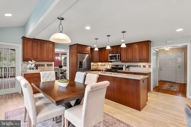 kitchen featuring light stone countertops, hanging light fixtures, an island with sink, tasteful backsplash, and appliances with stainless steel finishes