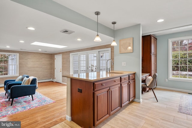 kitchen featuring light wood-type flooring, light stone counters, a baseboard heating unit, sink, and decorative light fixtures