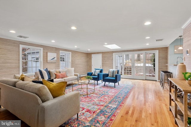 living room with a skylight, light hardwood / wood-style flooring, french doors, and crown molding