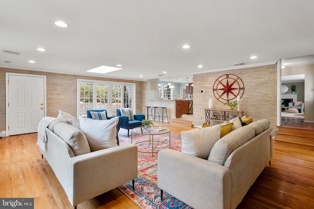 living room featuring a fireplace, a skylight, crown molding, and light hardwood / wood-style floors