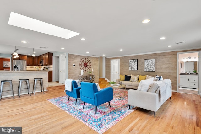 living room with ornamental molding, a skylight, and light hardwood / wood-style flooring