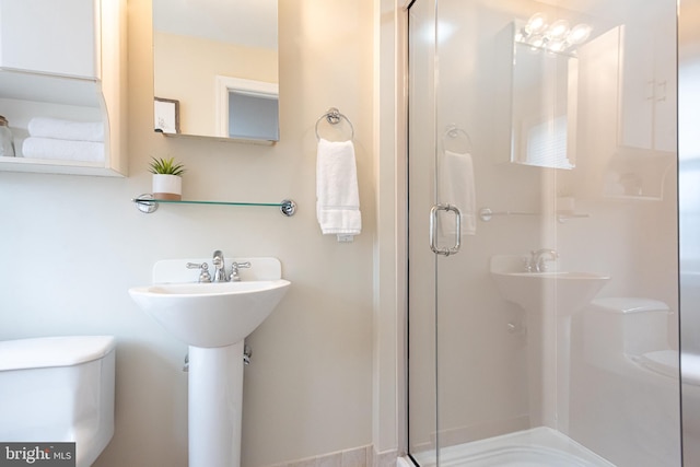 bathroom featuring toilet, sink, and a shower with shower door