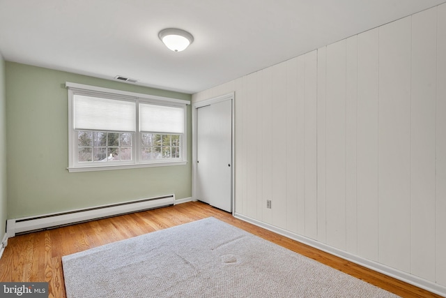 empty room featuring light wood-type flooring, wooden walls, and a baseboard heating unit