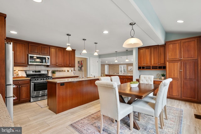 kitchen with stainless steel appliances, a kitchen island with sink, pendant lighting, and light hardwood / wood-style flooring