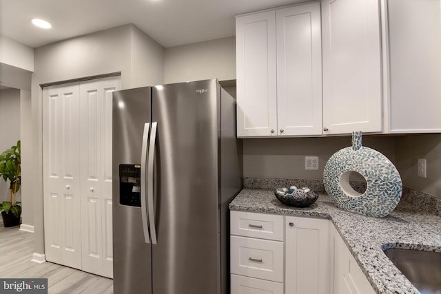 kitchen with white cabinets, light hardwood / wood-style floors, light stone counters, and stainless steel refrigerator with ice dispenser