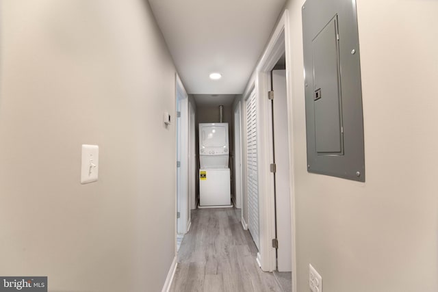 corridor with electric panel, stacked washer and dryer, and light hardwood / wood-style floors