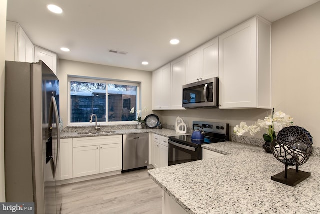 kitchen with white cabinetry, sink, light stone counters, appliances with stainless steel finishes, and light wood-type flooring