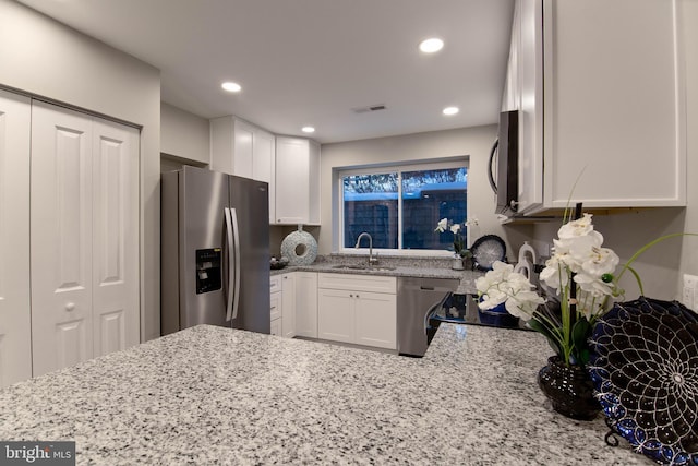 kitchen with light stone countertops, stainless steel appliances, white cabinetry, and sink