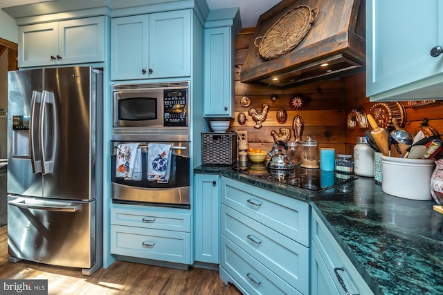 kitchen with blue cabinetry, dark hardwood / wood-style floors, custom range hood, and stainless steel appliances