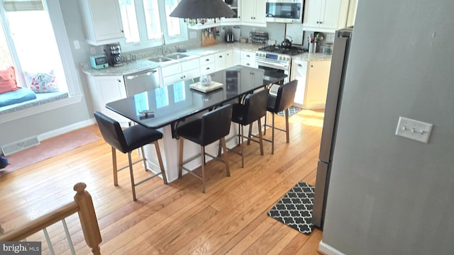 kitchen with white cabinetry, sink, light hardwood / wood-style flooring, a breakfast bar area, and appliances with stainless steel finishes