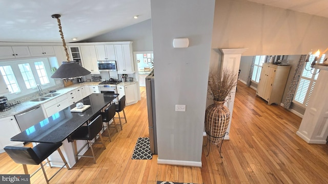 kitchen featuring white cabinetry, sink, hanging light fixtures, stainless steel appliances, and vaulted ceiling