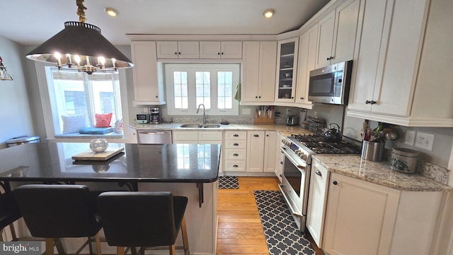 kitchen featuring pendant lighting, white cabinets, sink, light stone counters, and stainless steel appliances