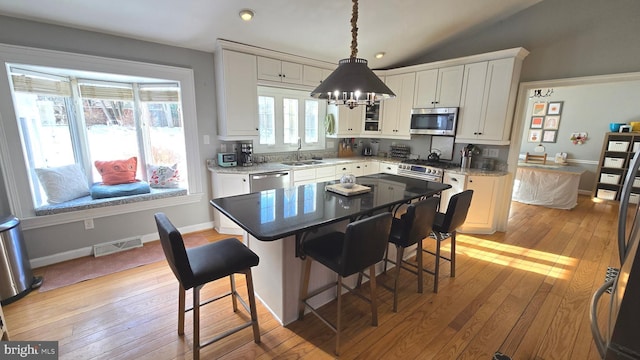 kitchen with lofted ceiling, a kitchen island, white cabinetry, and appliances with stainless steel finishes