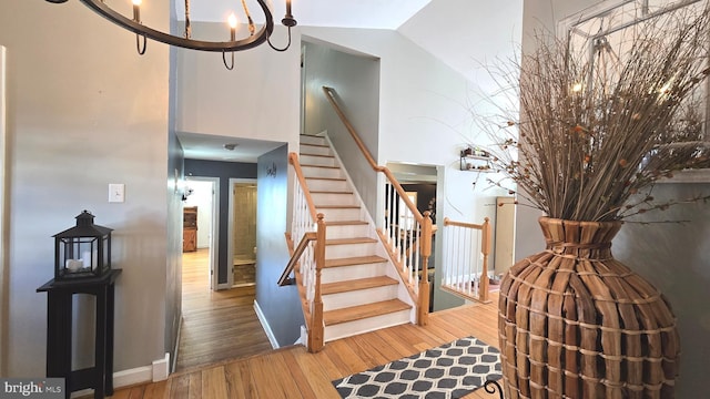 stairs with wood-type flooring, vaulted ceiling, and an inviting chandelier