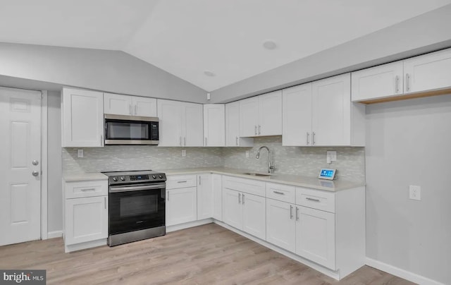 kitchen with appliances with stainless steel finishes, white cabinetry, lofted ceiling, and sink