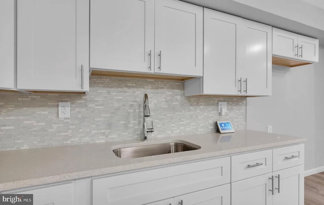 kitchen featuring white cabinets, backsplash, light stone countertops, and sink