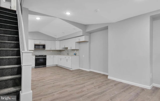 kitchen with white cabinetry, stainless steel appliances, light hardwood / wood-style flooring, vaulted ceiling, and decorative backsplash