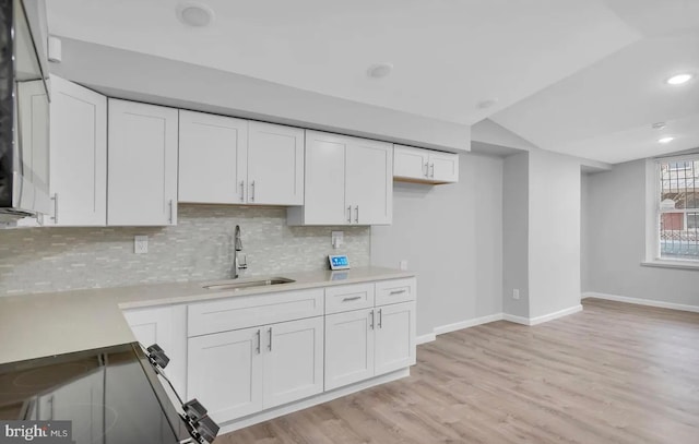 kitchen featuring sink, vaulted ceiling, decorative backsplash, white cabinets, and light wood-type flooring