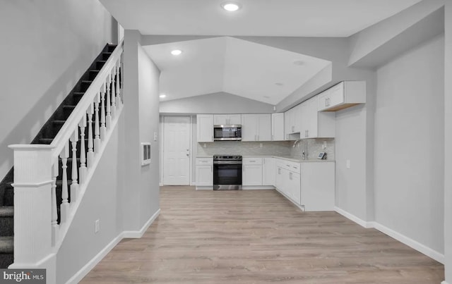 kitchen with tasteful backsplash, appliances with stainless steel finishes, lofted ceiling, white cabinets, and light wood-type flooring