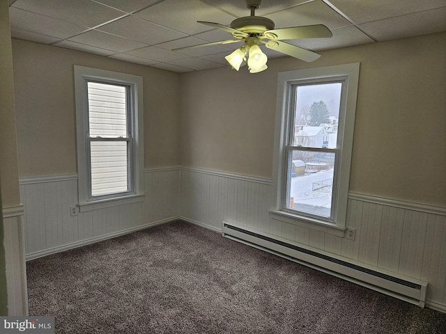 empty room with ceiling fan, carpet floors, a baseboard radiator, and a drop ceiling