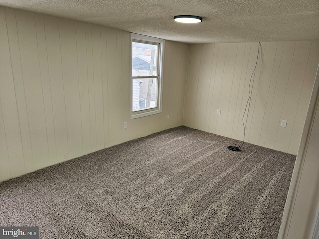 carpeted spare room featuring wood walls and a textured ceiling