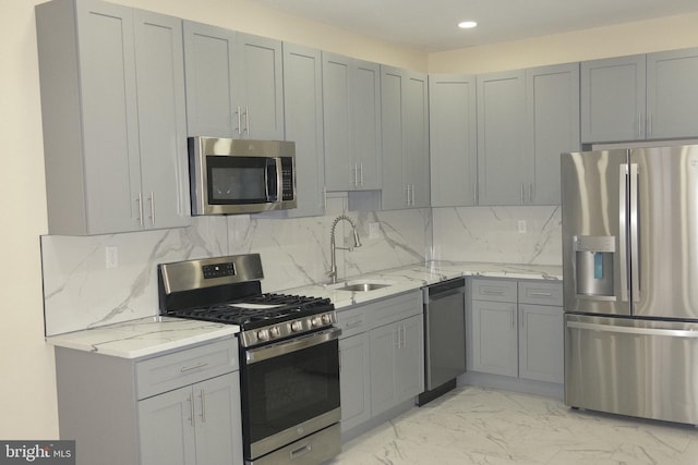 kitchen with gray cabinetry, appliances with stainless steel finishes, sink, and light stone counters