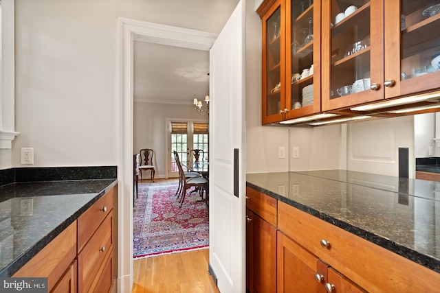 kitchen featuring a notable chandelier, dark stone countertops, ornamental molding, and light hardwood / wood-style flooring