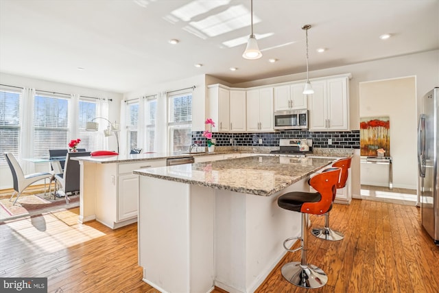 kitchen with stainless steel appliances, white cabinets, light stone counters, hanging light fixtures, and a kitchen island