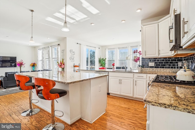 kitchen with white cabinets, hanging light fixtures, light stone countertops, and a kitchen island