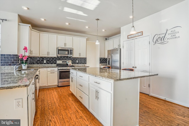 kitchen with a kitchen island, appliances with stainless steel finishes, pendant lighting, and white cabinetry