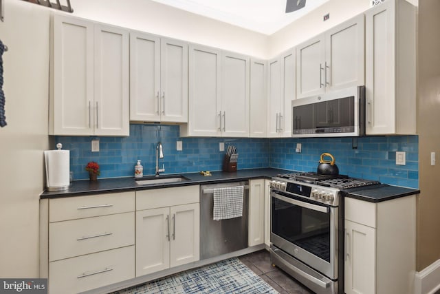 kitchen featuring backsplash, stainless steel appliances, dark tile patterned floors, sink, and white cabinets