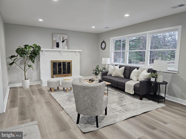 living room with a wealth of natural light, light hardwood / wood-style floors, and a brick fireplace