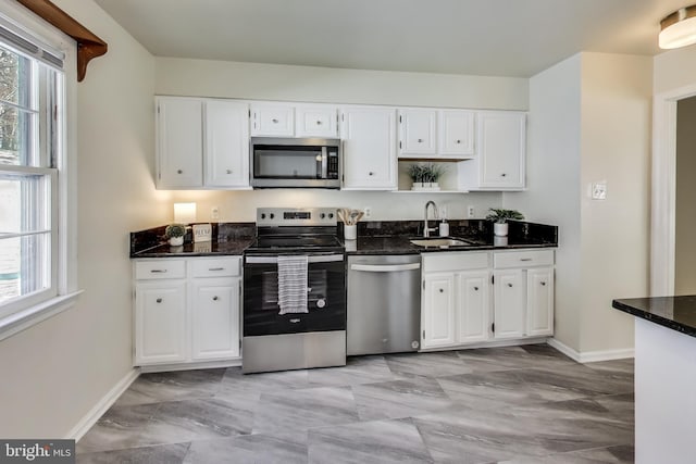 kitchen with appliances with stainless steel finishes, dark stone countertops, white cabinetry, and sink