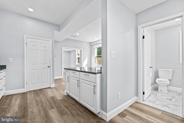 kitchen with white cabinets, light wood-type flooring, and dark stone counters