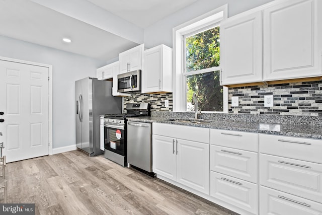 kitchen with sink, dark stone countertops, light hardwood / wood-style floors, white cabinets, and appliances with stainless steel finishes