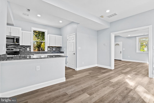 kitchen with backsplash, dark stone countertops, stove, and white cabinets