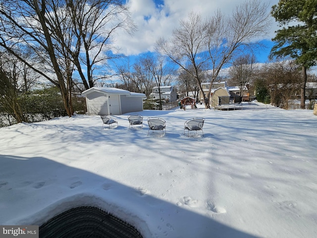 snowy yard featuring a trampoline and a storage unit