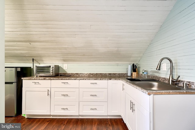 kitchen featuring stainless steel refrigerator, white cabinetry, sink, and lofted ceiling